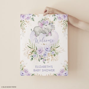 Puede incluir: Un cartel de bienvenida para una baby shower de color morado y dorado con una ilustraci&oacute;n de acuarela de un elefante durmiendo que lleva una corona de flores. El cartel dice "Bienvenido a la baby shower de Elizabeth".