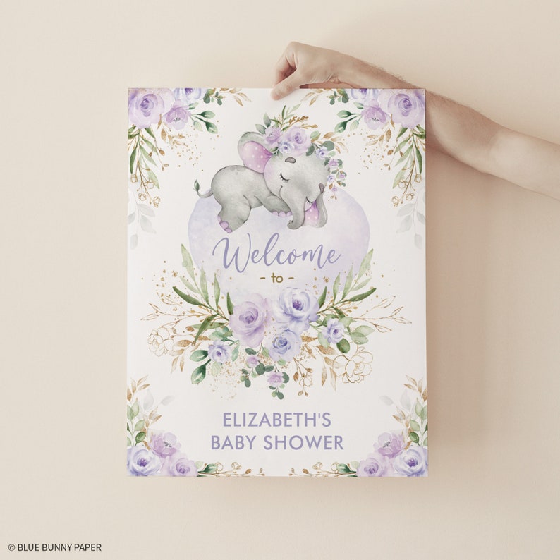 Puede incluir: Un cartel de bienvenida para una baby shower de color morado y dorado con una ilustraci&oacute;n de acuarela de un elefante durmiendo que lleva una corona de flores. El cartel dice "Bienvenido a la baby shower de Elizabeth".