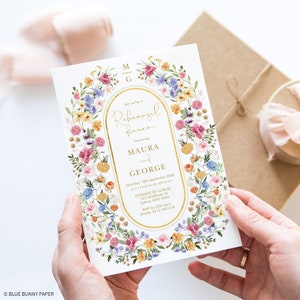 May include: A white invitation card with a gold border and floral design. The text reads "Join us for a Rehearsal Dinner honoring Maura and George. Saturday, 10th September 20XX at 4 o'clock in the afternoon. Domaine de la Rose 123 Wildflower St Sydney NSW 2345 RSVP by 25th April Amelia 0412 345 678"