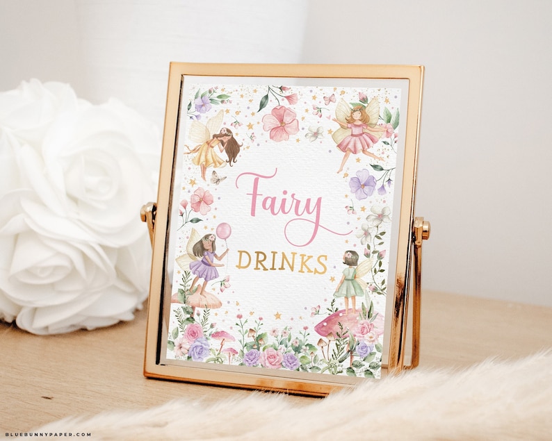 May include: A framed sign with the words "Fairy Drinks" in pink and gold script. The sign features watercolor illustrations of fairies, flowers, and butterflies. The frame is gold-colored and sits on a light-colored surface.