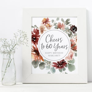 May include: A printable sign with a watercolor floral wreath in shades of red, pink, and green. The sign says "Cheers to 60 Years" and "Happy Birthday Margaret!"