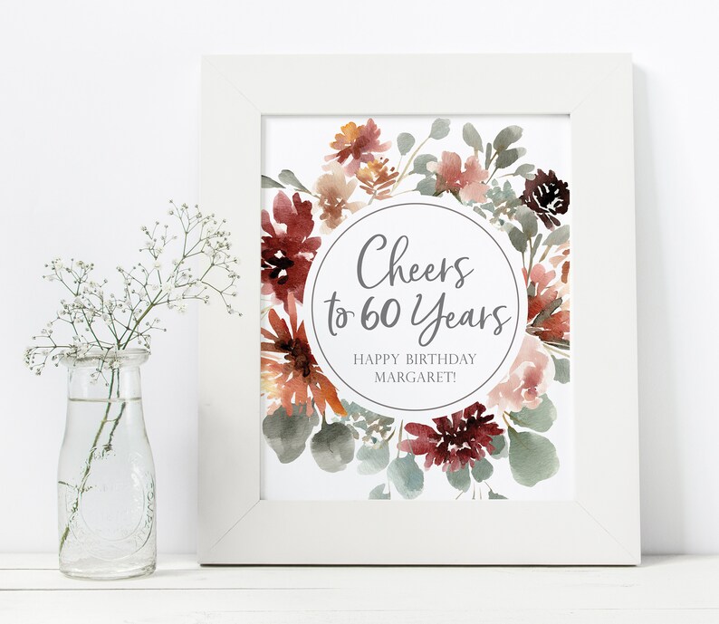 May include: A printable sign with a watercolor floral wreath in shades of red, pink, and green. The sign says "Cheers to 60 Years" and "Happy Birthday Margaret!"