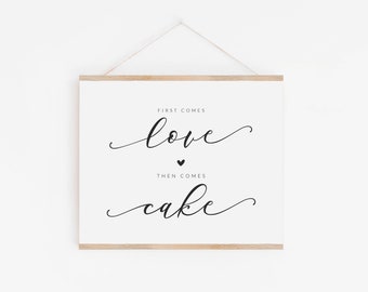 May include: A white sign with black text that reads "First comes love, then comes cake." The sign is hanging from a string and has a wooden frame.
