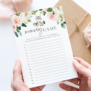 May include: A printable memory game card featuring a floral design and a cute kitten illustration. The card has the text "memory GAME" and instructions to list all the items you can remember. The guest who remembers the most items wins.