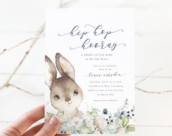 Puede incluir: Una invitación a una fiesta de bienvenida al bebé con una ilustración de acuarela de un conejito rodeado de flores azules y blancas. El texto dice "hip hop hooray" e incluye detalles sobre el evento, como la fecha, la hora, el lugar y la información de RSVP.
