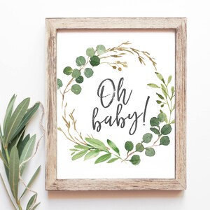May include: A framed print with a watercolor illustration of a green and gold wreath with the text "Oh baby!" in black script.