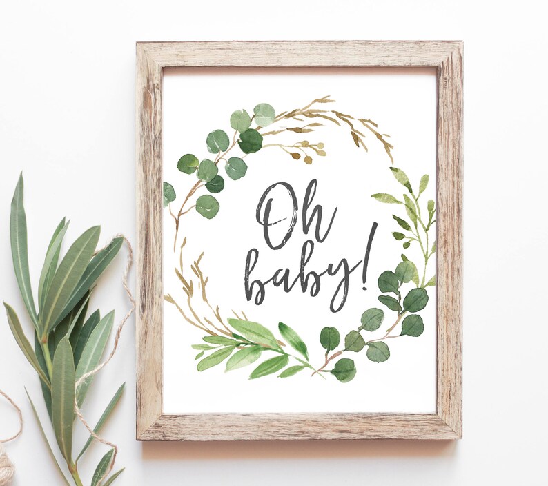 May include: A framed print with a watercolor illustration of a green and gold wreath with the text "Oh baby!" in black script.