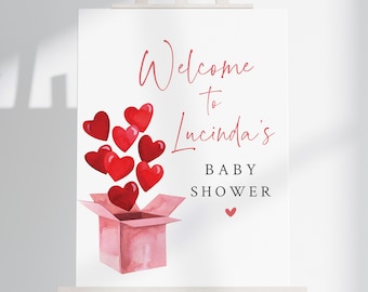 May include: Welcome to Lucinda's Baby Shower sign with a pink box and red hearts floating out of it.