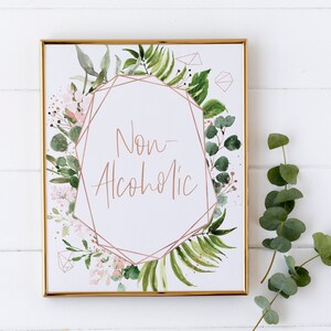 May include: A gold framed sign with a white background and a geometric design in rose gold. The sign has a floral border and the text "Non-Alcoholic" in rose gold calligraphy.