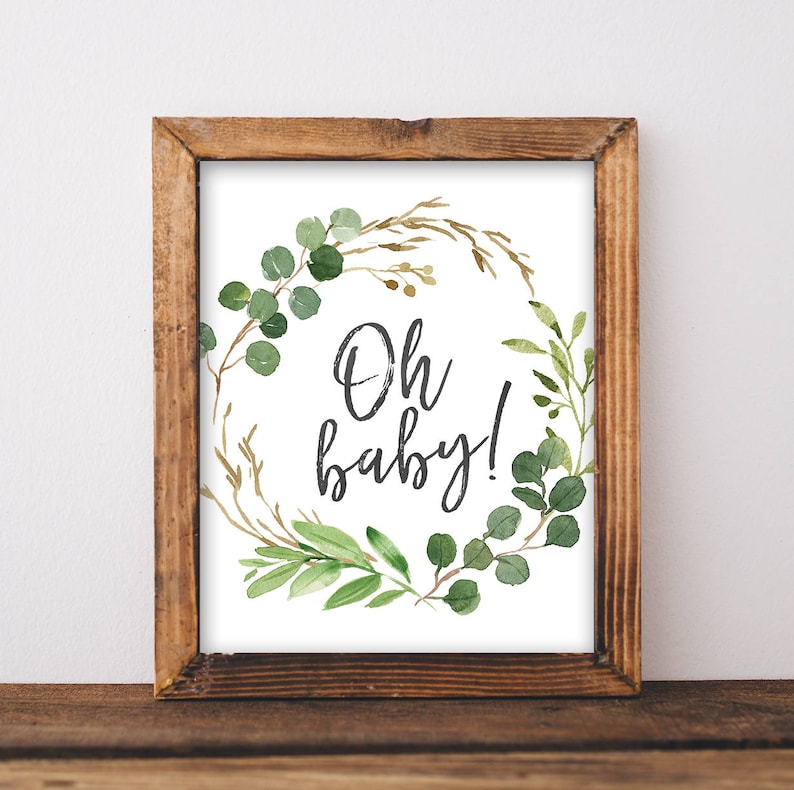 May include: A framed print with a green and brown watercolor wreath and the text "Oh baby!" in black script.
