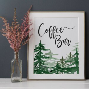 Puede incluir: Un cartel enmarcado en blanco con una ilustraci&oacute;n de acuarela de una escena de bosque. El cartel dice "Coffee Bar" en caligraf&iacute;a negra.