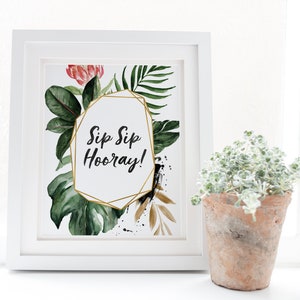 May include: A white framed print with a gold geometric frame and the text "Sip Sip Hooray!" surrounded by watercolor illustrations of tropical leaves and flowers.