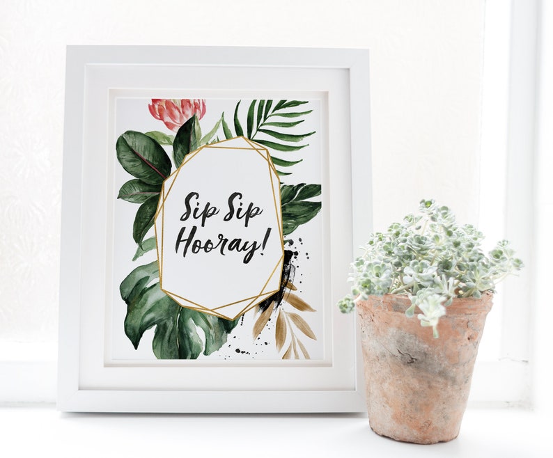 May include: A white framed print with a gold geometric frame and the text "Sip Sip Hooray!" surrounded by watercolor illustrations of tropical leaves and flowers.