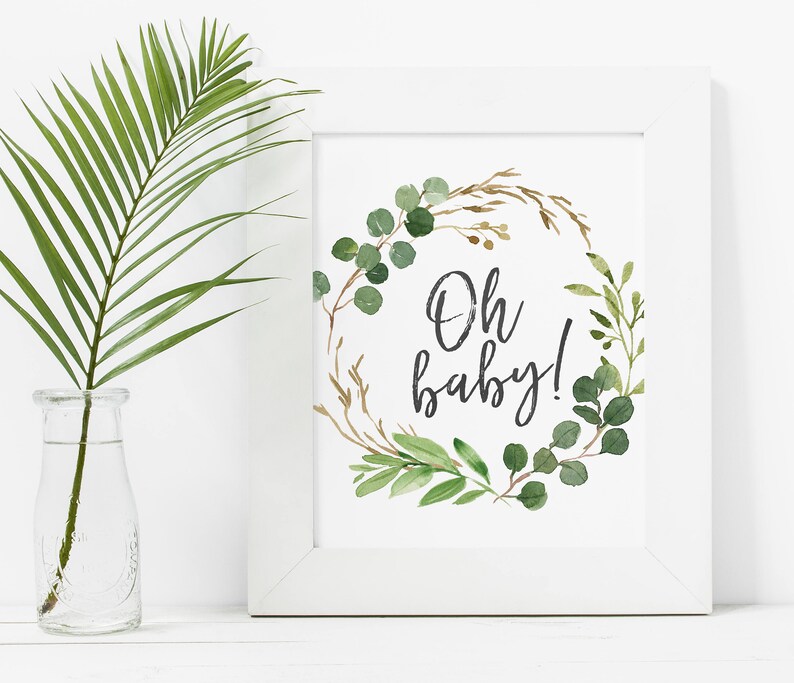 May include: A white framed print with a green and brown watercolor wreath with the text "Oh baby!" in black calligraphy.