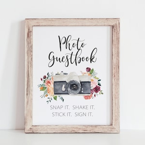 May include: A framed sign with the text "Photo Guestbook" and a watercolor illustration of a vintage camera with floral accents. The text below the image reads "Snap it. Shake it. Stick it. Sign it."