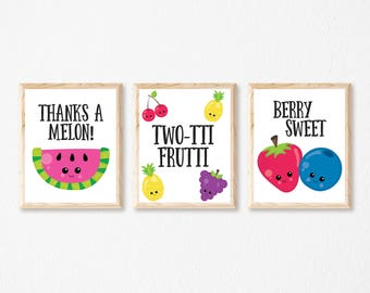 May include: Three framed prints with fruit illustrations and puns. The first print has a watermelon with the text "Thanks a Melon!" The second print has a pineapple, cherries, and grapes with the text "Two-tti Frutti". The third print has a strawberry and blueberry with the text "Berry Sweet".