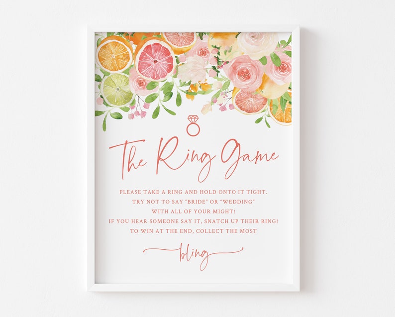 May include: A printable bridal shower game sign with a watercolor illustration of pink flowers, green leaves, and citrus fruit slices. The text reads "The Ring Game" and includes instructions for the game.