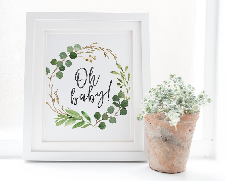 May include: White framed print with a watercolor illustration of a green and gold leafy wreath with the text "Oh baby!" in black calligraphy.