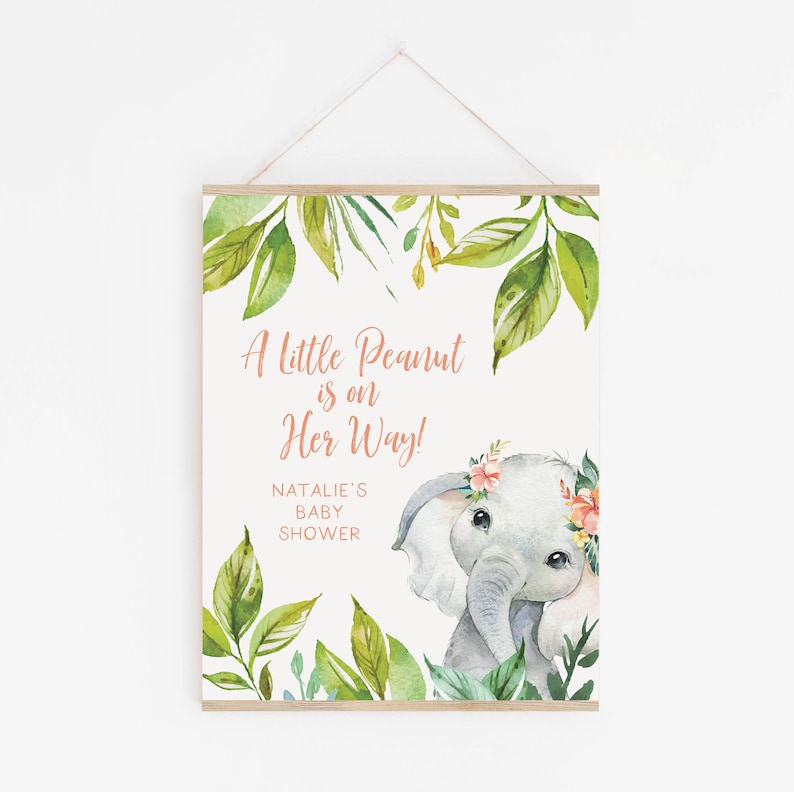 May include: A baby shower sign featuring an illustration of a gray elephant wearing a floral crown. The sign includes the text "A little Peanut is on Her Way!" and "Natalie's Baby Shower" with green leaf accents.