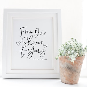 May include: White framed sign with black calligraphy that reads "From Our Shower to Yours" with two small hearts on either side of the word "Shower". The sign also says "Please Take One" in smaller font below the calligraphy.