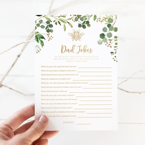 May include: A printable game card with a green and gold floral design. The card features the text "Dad Jokes" and a list of questions and answers for a game.