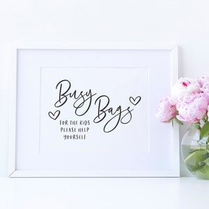 May include: White framed sign with black text that reads "Busy Bags" with two hearts. The text below reads "For the kids please help yourself".