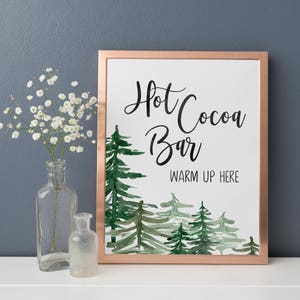 May include: A printable sign with a copper frame and a watercolor illustration of pine trees. The sign reads "Hot Cocoa Bar Warm Up Here".