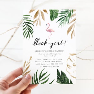 Könnte beinhalten: Eine tropische Hochzeitseinladung mit einem rosafarbenen Flamingo und goldenen und grünen Palmenblättern. Der Text lautet "flock yeah!" und enthält den Namen der Braut, das Hochzeitsdatum, die Uhrzeit, den Ort und die RSVP-Informationen.