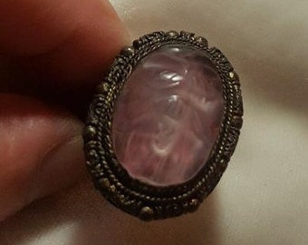 Peut inclure: Une bague en argent avec un camée ovale rose orné d'un motif sculpté. Le camée est serti dans une bélière en argent avec une bordure décorative.