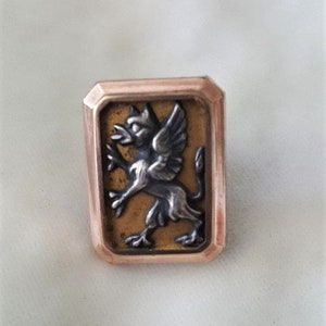 May include: A gold-toned rectangular ring featuring a raised, detailed silver-toned griffin design.