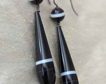 May include: A pair of silver dangle earrings with black and white agate teardrop-shaped stones. The stones have a white stripe across the center.