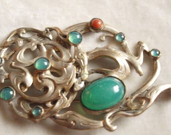 Peut inclure: Une broche en argent avec un design complexe présentant un motif en spirale et plusieurs pierres précieuses de couleur verte et corail.