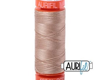May include: A spool of Aurifil 100% cotton thread in a light beige color. The spool is labeled "Aurifil Mako 100% Cotton" and "100% Cot".