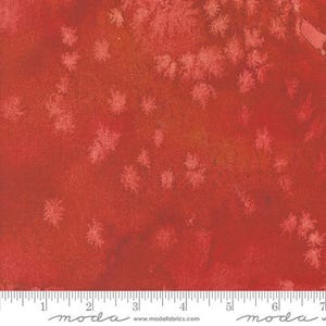 May include: Red fabric with a subtle white speckled pattern. The fabric has a textured surface and a slightly faded look. The fabric is shown with a ruler for scale.