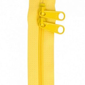 May include: A bright yellow zipper with two pulls. The zipper is closed and has a double-pull design. The zipper teeth are visible, and the fabric is a solid yellow color. The zipper is against a white background.