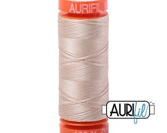 May include: A spool of Aurifil 100% cotton thread in a light beige color. The spool is labeled "Aurifil" and "100% Cotton".