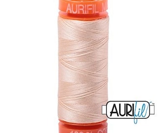 May include: A spool of Aurifil thread in a light peach color. The thread is tightly wound around a cylindrical core. The spool has orange caps with the Aurifil logo and "100% CO" printed on them. The thread is designed for sewing and quilting projects.