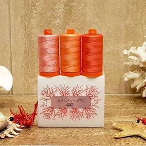 May include: Three spools of coral-colored thread in a white box with a coral design and the text "2019 Coral Palette Aurifil".