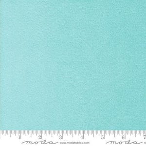 May include: A close-up of a solid, light turquoise fabric with a textured surface. A ruler with inch markings is at the bottom. The fabric is likely used for quilting or other sewing projects.