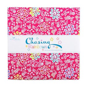 May include: A square stack of fabric squares featuring a vibrant hot pink background with a repeating pattern of white, yellow, light blue, and purple flowers. A white paper band wraps around the center with the text Chasing Rainbows.