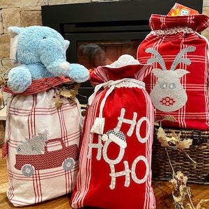 May include: Three red and white plaid Christmas gift bags. One bag has a reindeer applique, one has a truck and Christmas tree applique, and one has the words "HO HO HO" in white.
