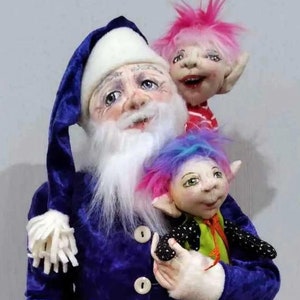 Könnte beinhalten: Eine skurrile Weihnachtsmann-Puppe mit einem blauen Samtanzug, weißem Bart und passendem Hut. Zwei Elfenpuppen mit rosa und blauem Haar sitzen auf dem Weihnachtsmann. Die Elfenpuppen haben bemalte Gesichter und tragen bunte Outfits. Die Weihnachtsmann-Puppe hält eine der Elfenpuppen.