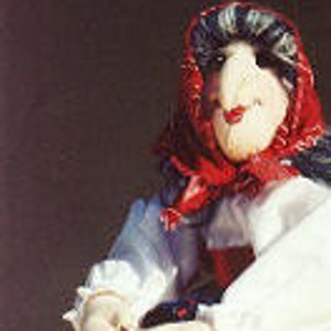 Puede incluir: Una muñeca de tela hecha a mano vestida con una falda a cuadros rojos y blancos, una blusa blanca y un pañuelo rojo, montando una escoba de alambre.