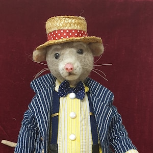 May include: A gray felt mouse wearing a straw hat with a red and white polka dot band, a blue and white striped jacket, a yellow and white striped shirt, a blue bow tie, yellow pants with a floral pattern, and black shoes with yellow laces.