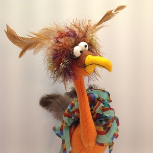 May include: A whimsical orange bird with a colorful scarf and large googly eyes. The bird has brown feathers and long, striped legs.