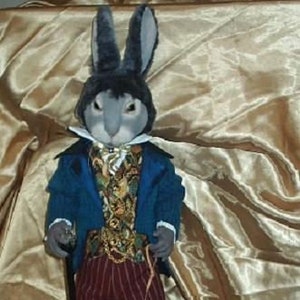 May include: A whimsical doll of a rabbit dressed in a blue jacket, patterned vest, and striped pants, holding a cane and a leash attached to a turtle. The rabbit has a gray face and ears. The turtle has a patterned shell.