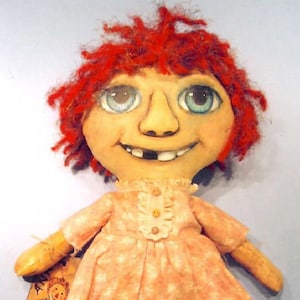 May include: A handmade rag doll with red yarn hair, a pink and white floral dress, and striped stockings. The doll has a painted face with blue eyes and a toothy grin.