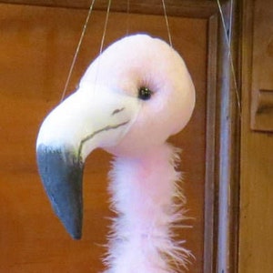 Può includere: Un pupazzo di fenicottero rosa con piume bianche e un collo lungo e sottile. Il pupazzo ha un becco nero e gambe bianche.