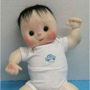 May include: A handmade cloth doll with black hair, wearing a white onesie with a blue car graphic and the text "zoom".