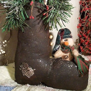 May include: A brown boot-shaped Christmas stocking with a snowman figurine inside. The stocking is decorated with a green and red garland and bells.